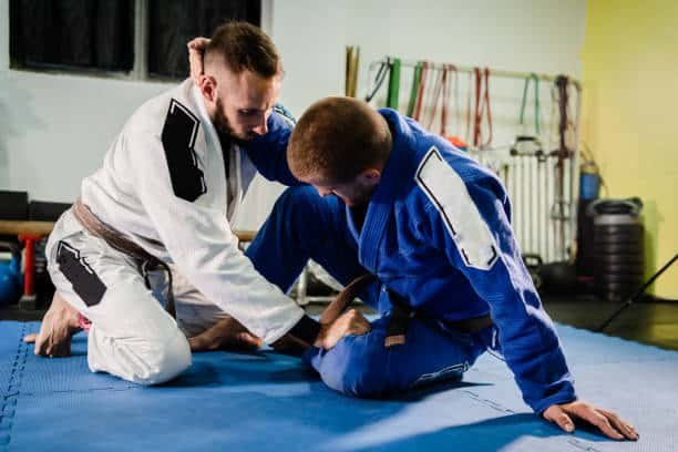 جلسة جوجيتسو الرياض، تدريب BJJ للفنون القتالية، نزال في الأكاديمية بين مقاتلين في وضعية "بترفلاي جارد" (الحارس الفراشة)، تدريبات على التقنيات وممارسة بالـ "جي" (الكيمونو).